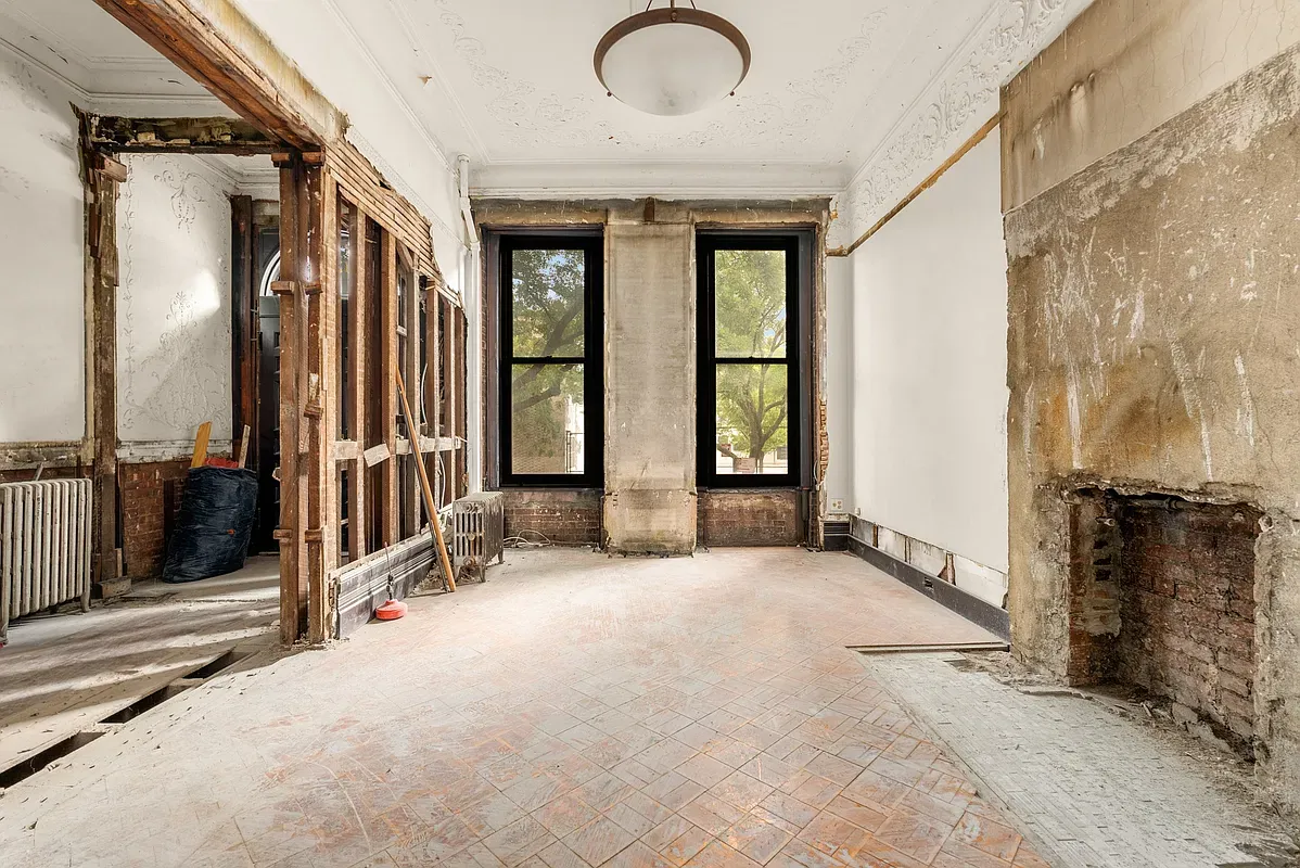 Unrenovated parlor room with tall windows and exposed fireplace at 128 West 121st Street