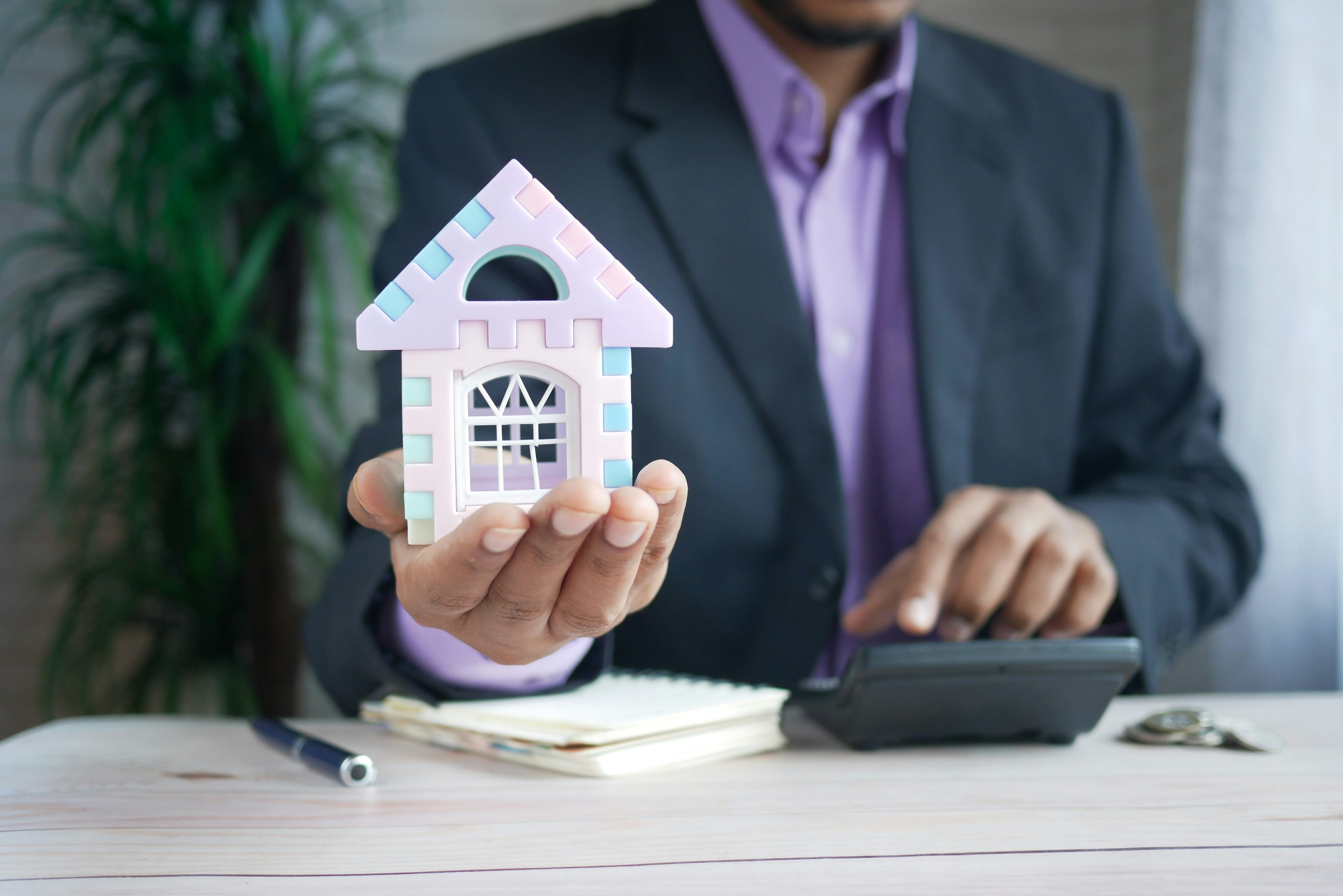 NYC mortgage concept with real estate agent holding house model and calculating home loan costs on a calculator